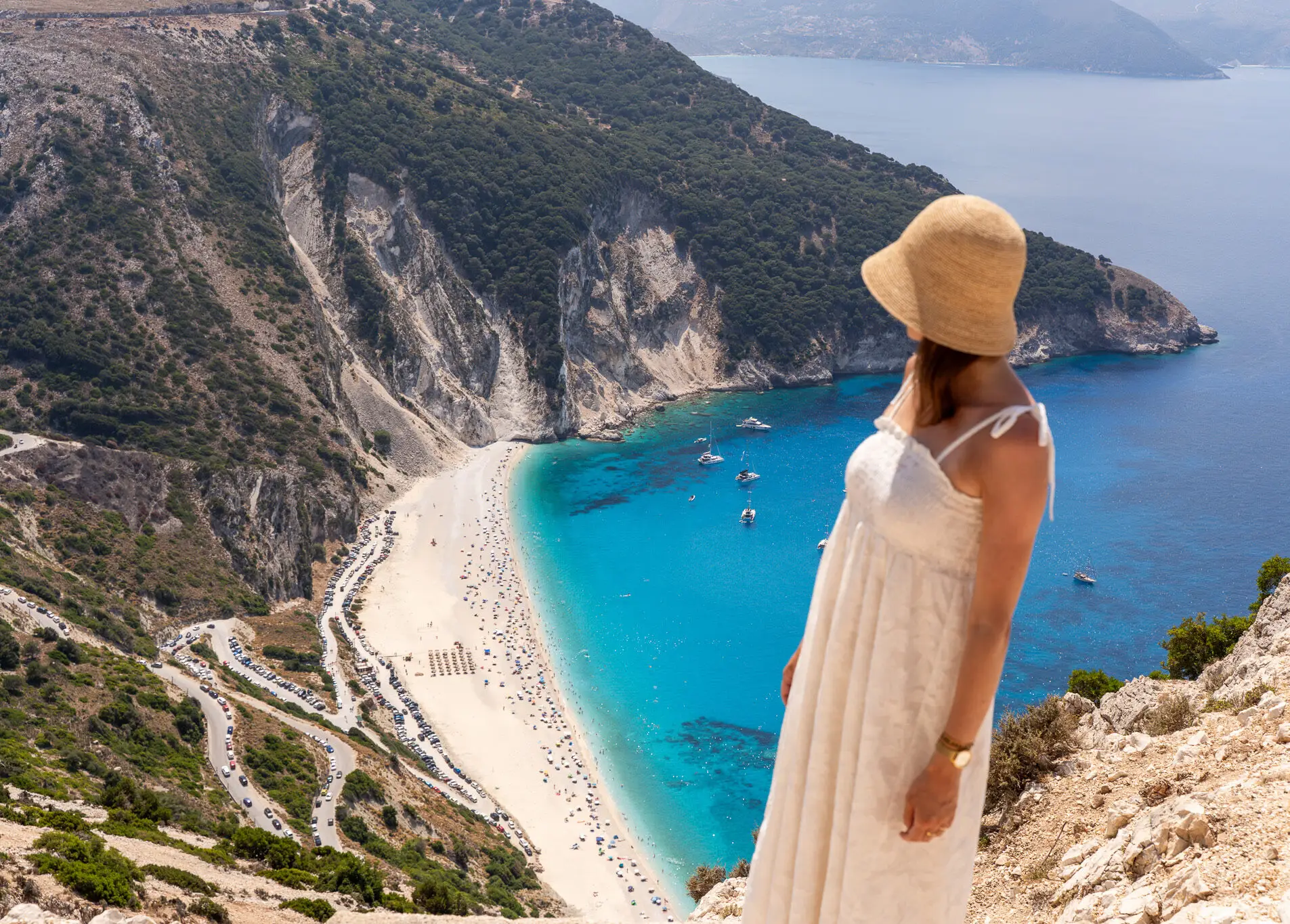Piękna kobieta w podróży w białej sukni patrzy na słynną plażę Myrtos (Kefalonia, Grecja) z turkusowym morzem w okresie letnim podczas wycieczki fakultatywnej z Zakynthos z przewodnikiem