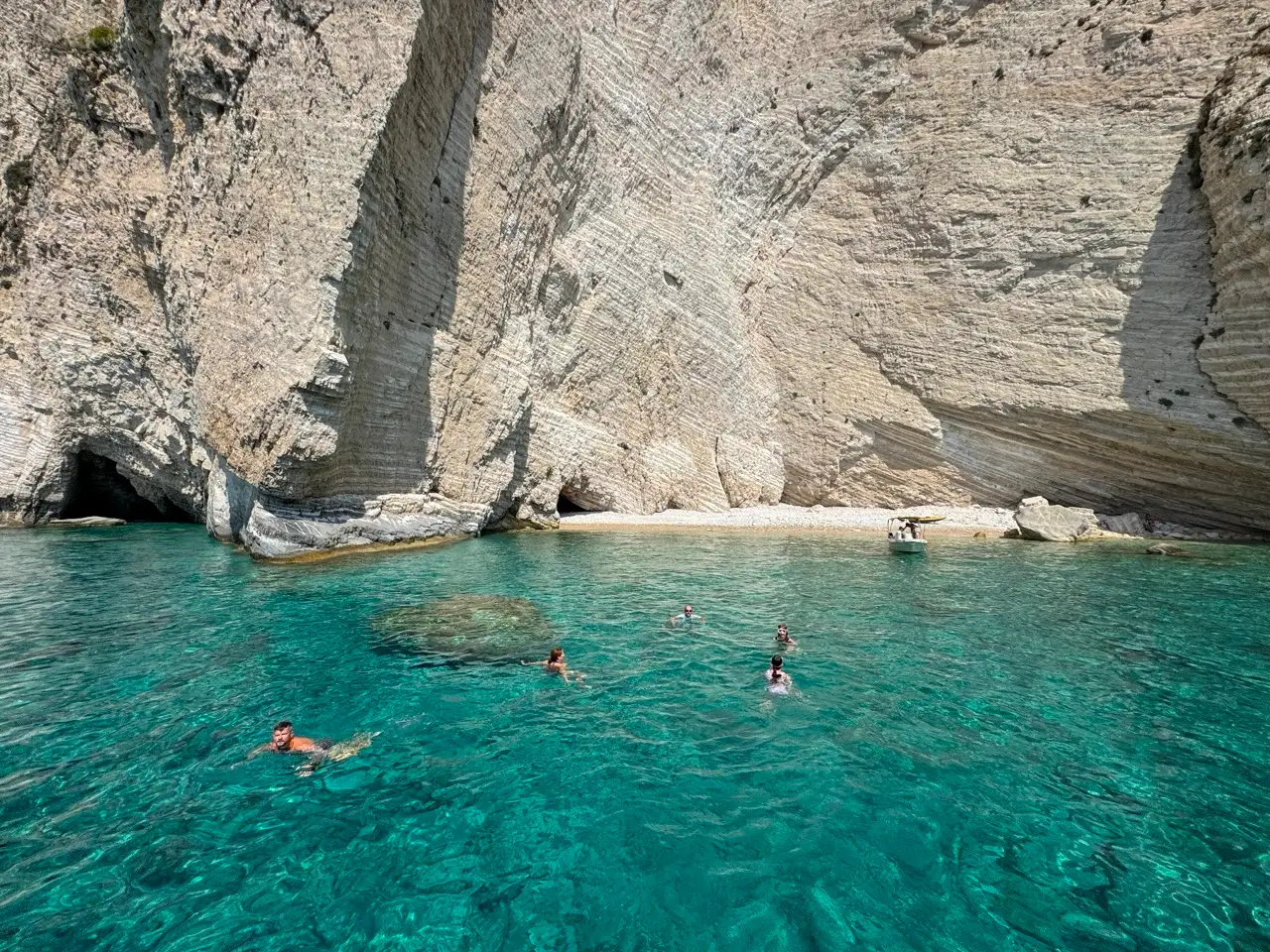 Turyści pływający w krystalicznie czystej wodzie u stóp wapiennych klifów Zakynthos podczas przystanku kąpielowego ze statku.