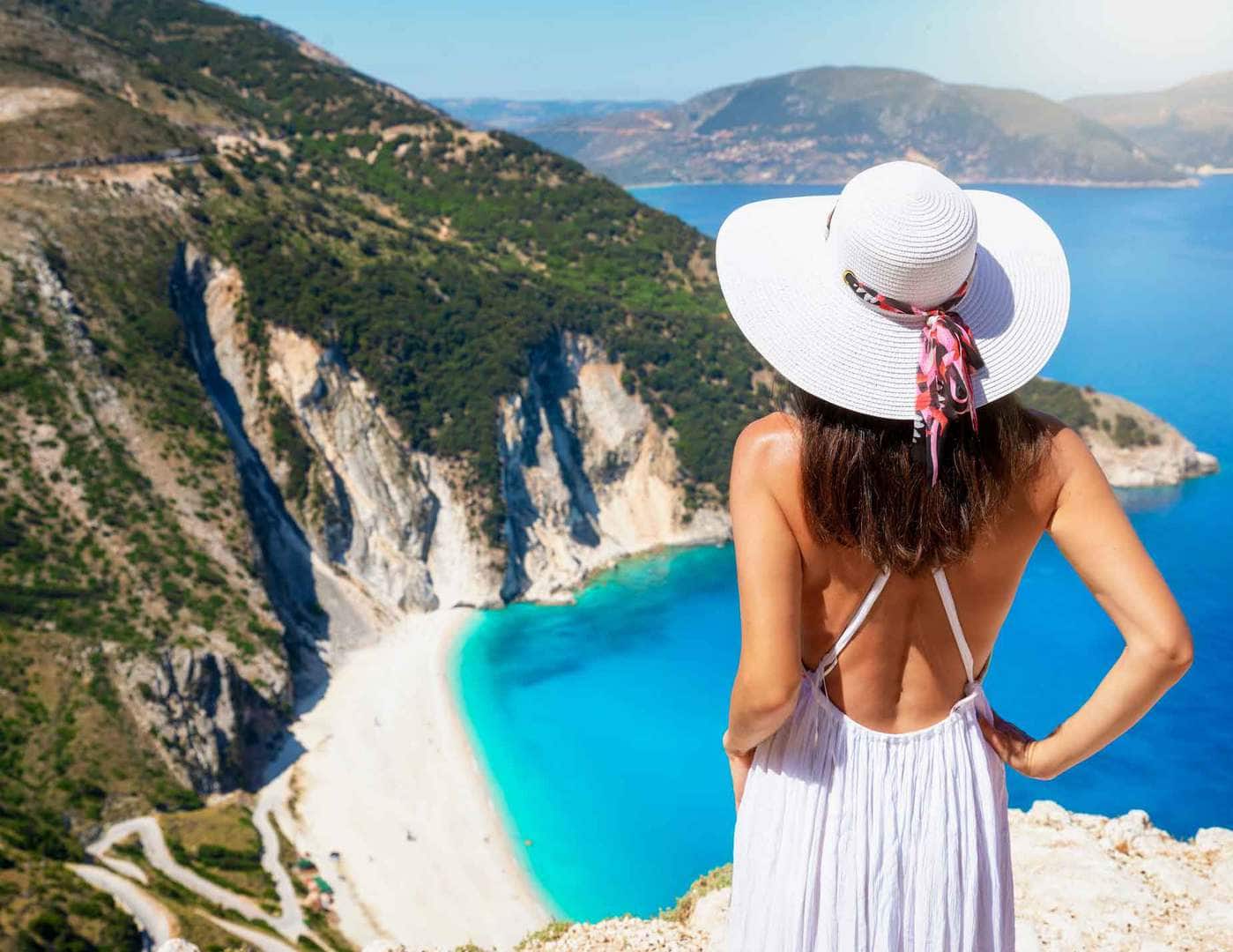 Piękna kobieta w podróży w białej sukni patrzy na słynną plażę Myrtos (Kefalonia, Grecja) z turkusowym morzem w okresie letnim podczas wycieczki fakultatywnej z Zakynthos z przewodnikiem