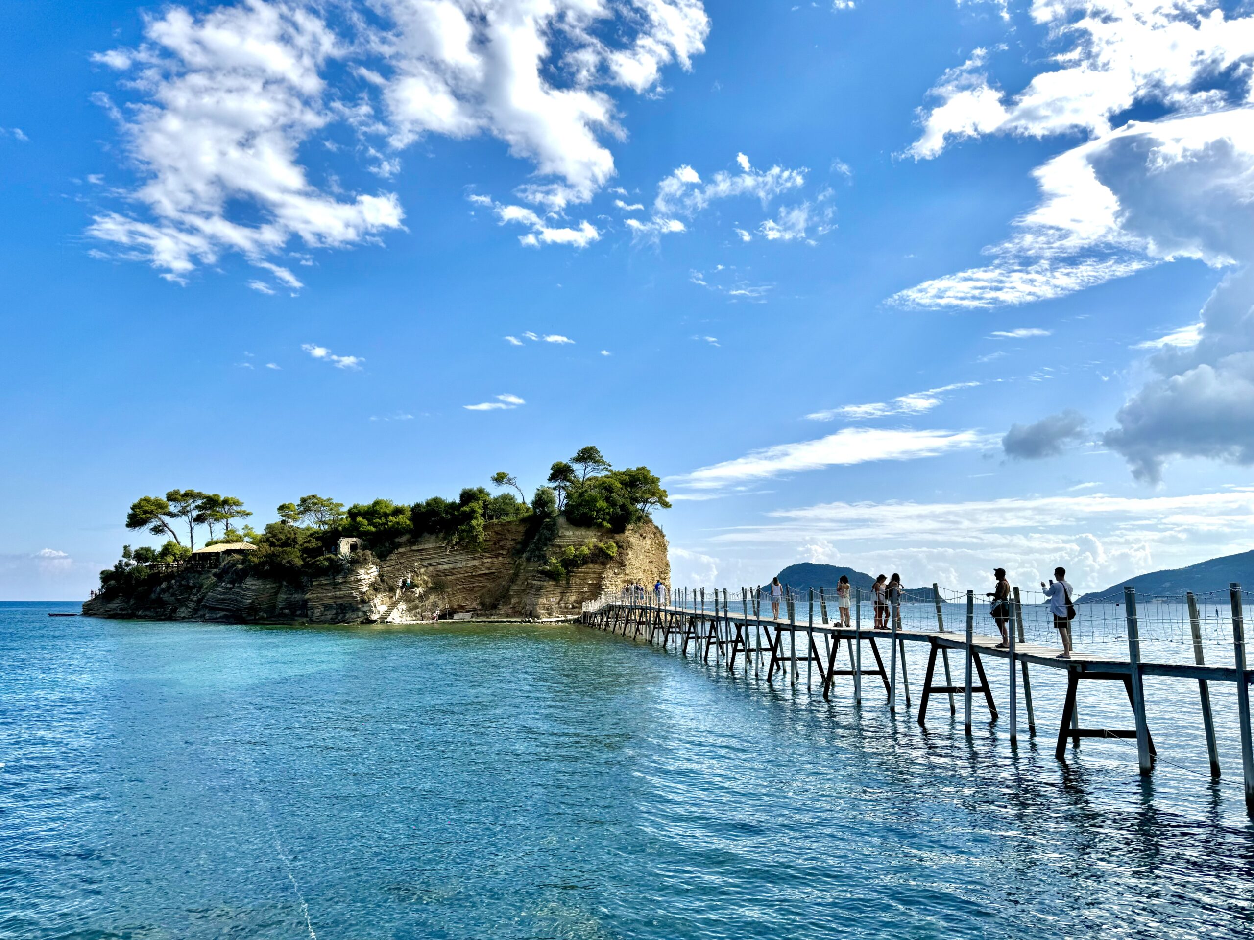 Most prowadzący z portu Agios Sostis na wyspę Cameo na Zakynthos, z turkusowym morzem i błękitnym niebem w tle.