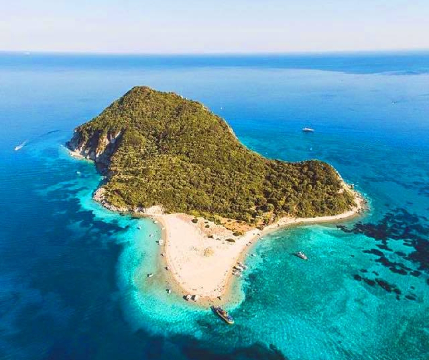 Zielona bezludna wyspa Marathonisi w kształcie żółwia otoczona błękitnym morzem. Zdjęcie z góry, z drona
