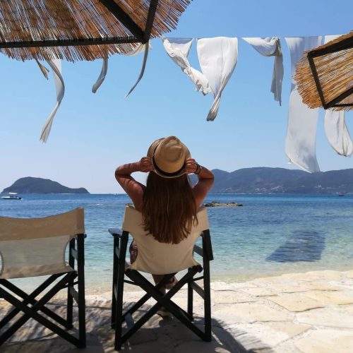 Kobieta siedząca na rozkładanym krześle na malowniczej plaży na wysepce ślubów Cameo - Agios Sostis w Grecja