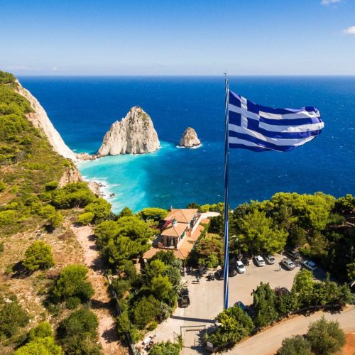 Wielka grecka flaga na przylądku Keri na Zakynthos w słoneczy letni dzień ze skałami Mizithres w oddali Grecja wycieczki fakultatywne po polsku